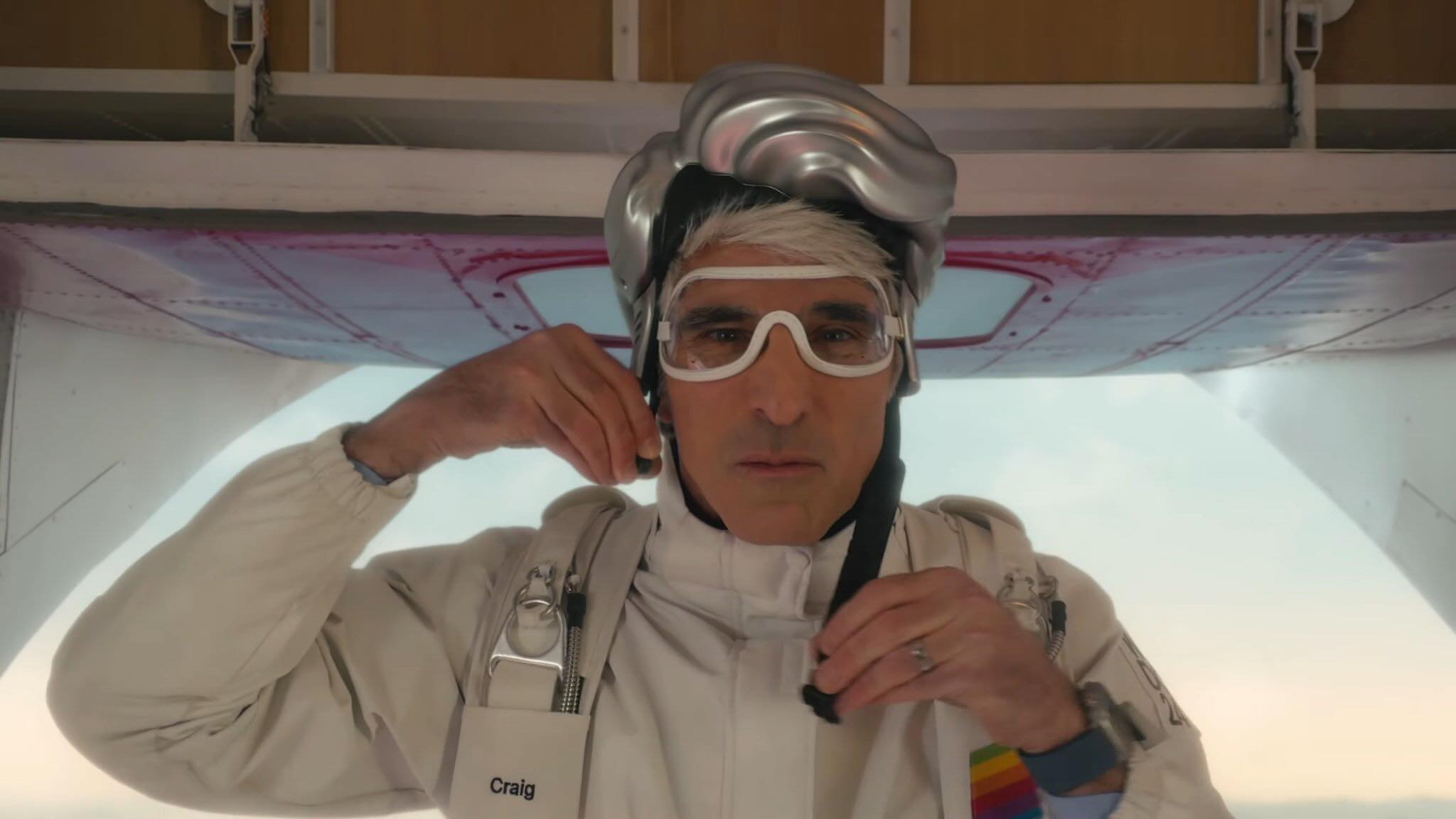 Craig Federighi con un casco de plástico que simula su pelo antes de tirarse de un Avión para hacer paracaidismo en el vídeo de apertura de la WWDC 2024