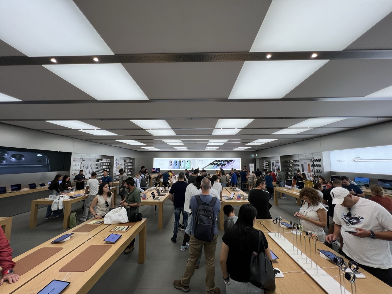 La gente haciendo cola en una Apple Store, con carteles del iPhone 17 de fondo